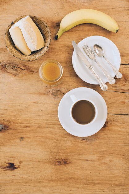 Una vista elevada del pan; taza de café; mermelada; Pan y plátano para el desayuno.