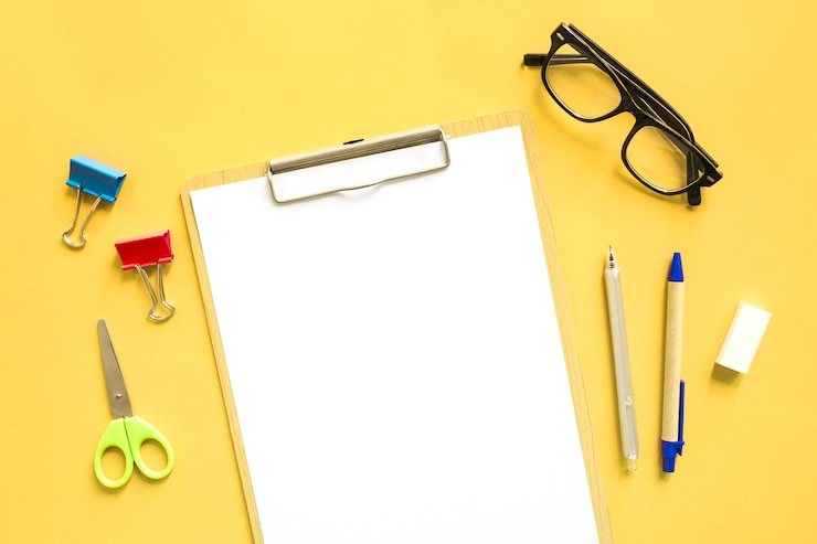 Foto gratuito vista elevada de papel blanco en blanco cerca de papelerías sobre fondo amarillo