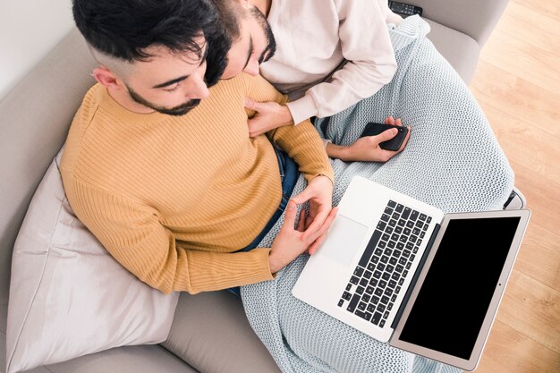 Una vista elevada de una pareja homosexual joven sentada en un sofá mirando una tableta digital