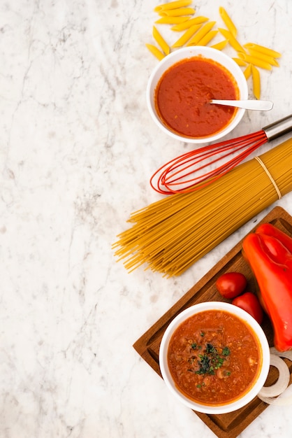 Vista elevada de pasta cruda y salsa de tomate sobre fondo de mármol con textura