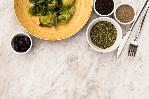 Vista elevada de pasta de ravioles verdes e ingredientes crudos sobre fondo con textura de mármol