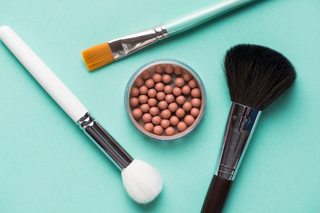 Foto gratuita una vista elevada de perlas bronceadas dentro de los tres pinceles de maquillaje