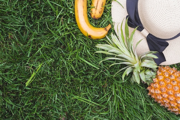 Foto gratuita vista elevada de piña; plátano y sombrero en la hierba verde