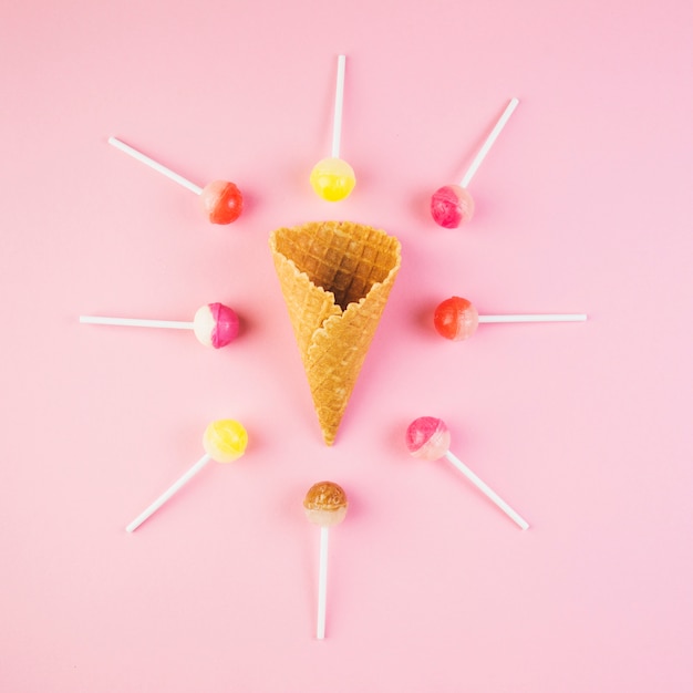 Vista elevada de piruletas rodeadas de helado de cono de galleta en superficie rosada