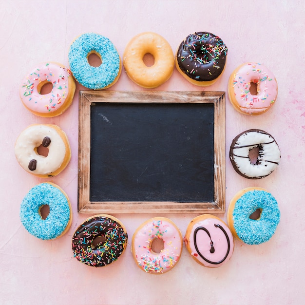 Foto gratuita vista elevada de pizarra negra en blanco rodeada por varias rosquillas