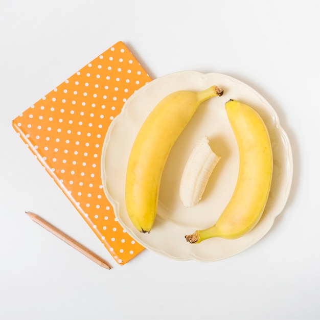 Vista elevada de plátanos; cuaderno y lápiz sobre fondo blanco