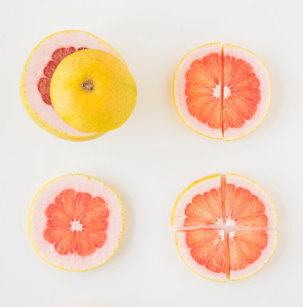 Una vista elevada de pomelo cortado en diferentes rodajas sobre fondo blanco