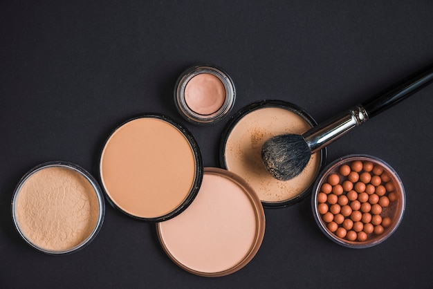 Vista elevada de productos de maquillaje y pincel sobre superficie negra