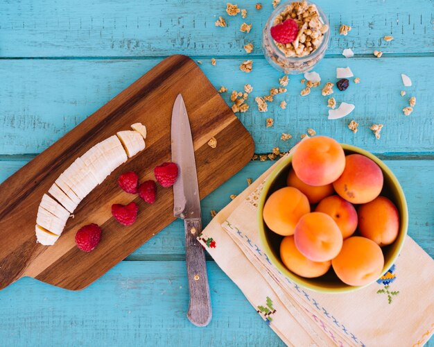 Vista elevada de rodajas de banana; fresas; melocotón y avena en el fondo de madera azul