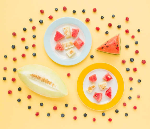 Foto gratuita una vista elevada de rodajas de melón y sandía decoradas con arándanos y frambuesas sobre fondo amarillo