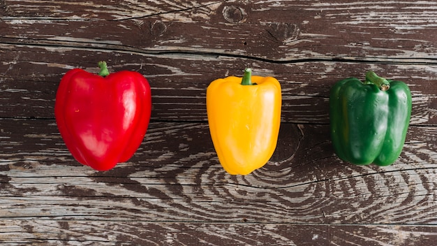 Una vista elevada de rojo; Pimientos amarillos y verdes en superficie de madera dañada