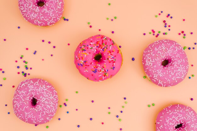 Una vista elevada de rosquillas rosadas con bolas asperjadas sobre fondo coloreado