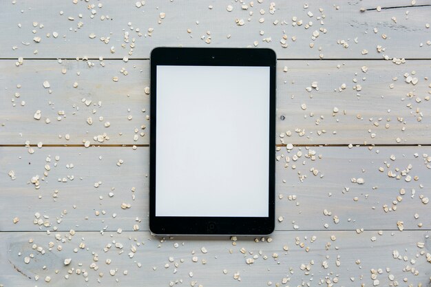 Vista elevada de la tableta digital con avena dispersa en un tablón de madera