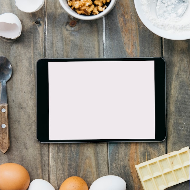 Foto gratuita vista elevada de la tableta digital rodeada de varios ingredientes en el escritorio