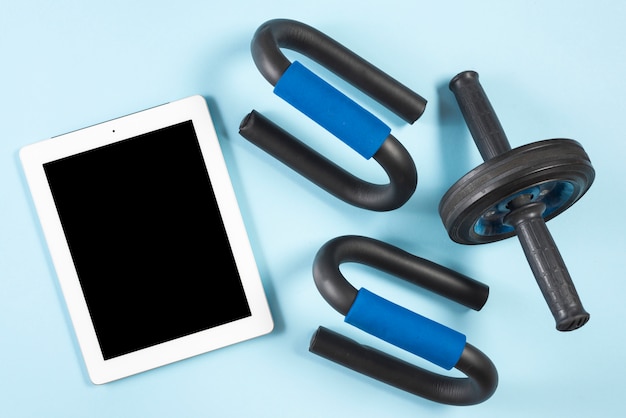 Una vista elevada de la tableta digital con rodillo de fitness y barra de empuje hacia arriba sobre fondo azul