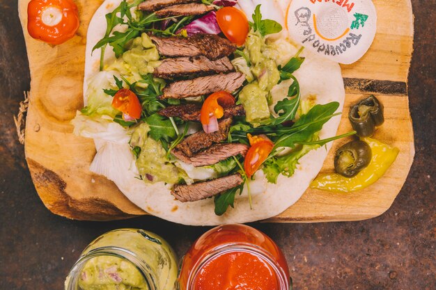 Vista elevada de tacos mexicanos con carne de res en una tabla de cortar con frascos de guacamole y salsa de salsa