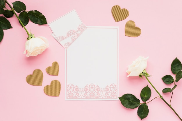 Foto gratuita vista elevada de tarjetas en blanco con corazones dorados y rosas en superficie rosada