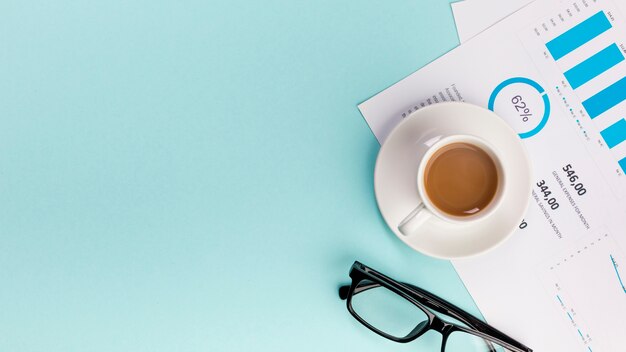 Una vista elevada de la taza de café en el plan de presupuesto de negocios y anteojos sobre fondo azul