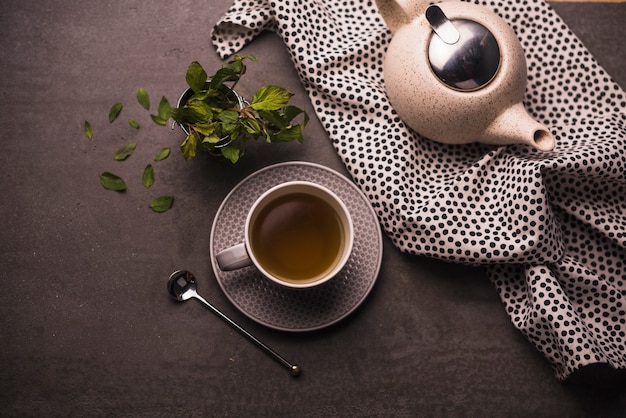 Vista elevada del té; hojas; Tetera y lunares textiles en la mesa.