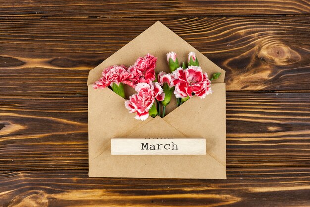 Vista elevada del texto de marzo en el bloque de madera sobre sobre con flores rojas