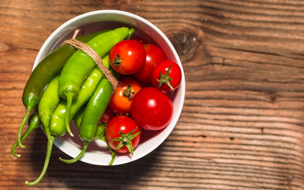 Foto gratuita vista elevada de tomates cherry y chiles verdes en superficie de madera