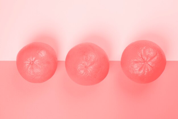 Una vista elevada de tres pomelos enteros sobre fondo rosa