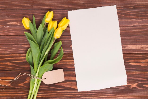 La vista elevada del tulipán amarillo florece con el papel en blanco sobre fondo texturizado de madera