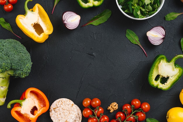 Una vista elevada de verduras frescas y pastel de arroz inflado sobre fondo negro de concreto