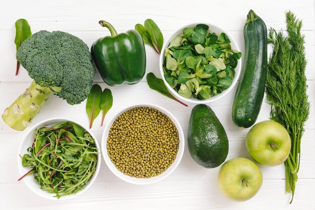 Una vista elevada de verduras frescas saludables; frijol mungo y manzana en mesa blanca