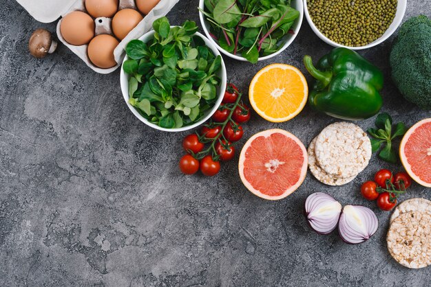 Una vista elevada de las verduras; huevos; Pastel de cítricos y arroz inflado sobre fondo de hormigón gris