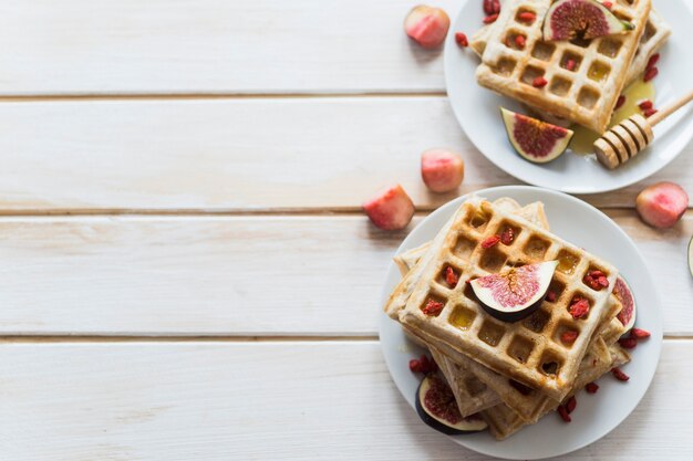 Vista elevada de waffles belgas; higo; miel; y cazo de miel servido en placa sobre tablón de madera