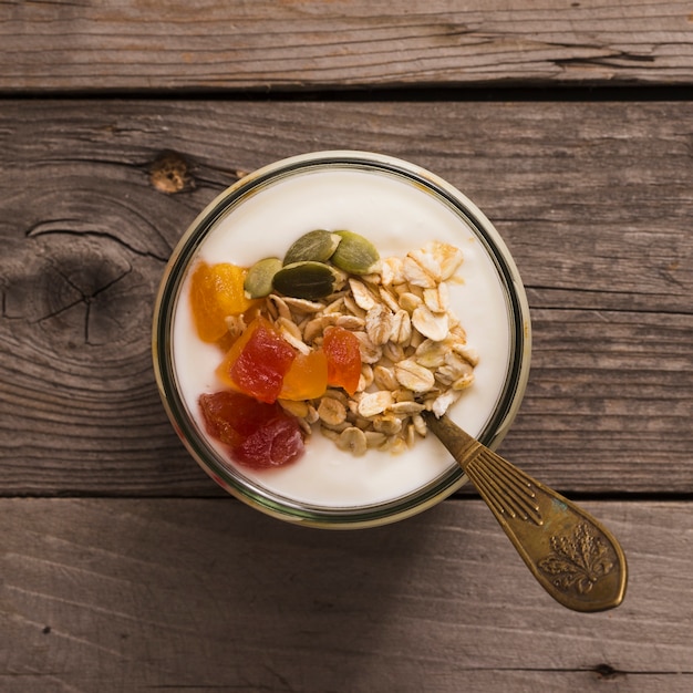 Vista elevada de yogur con muesli, semillas de calabaza y frutas en la rústica mesa de madera