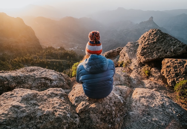 Foto gratuita una vista fascinante de las montañas rocosas desde la cima y una mujer sentada al revés