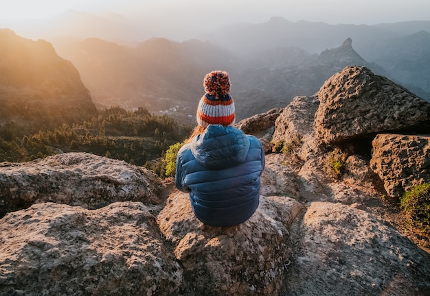 Una vista fascinante de las montañas rocosas desde la cima y una mujer sentada al revés