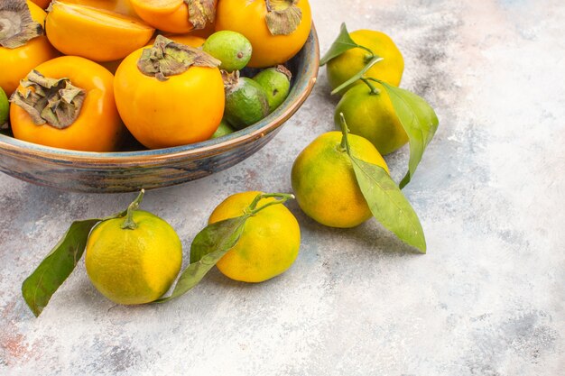 Vista fresca feijoas de caquis frescos en un cuenco y mandarinas sobre fondo desnudo espacio libre