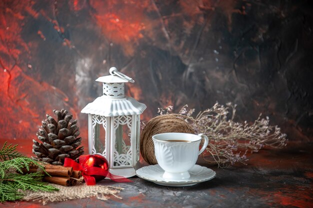 Vista frontal de los accesorios de decoración cono de coníferas una bola de cuerda y ramas de abeto limones de canela una taza de té sobre fondo oscuro