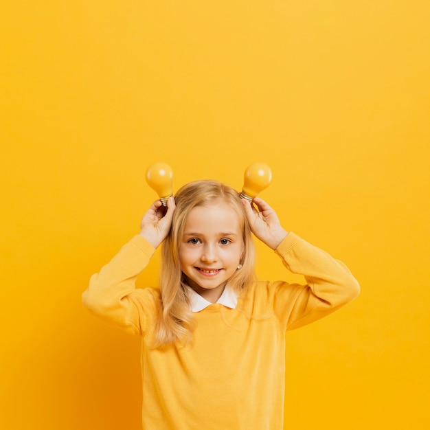 Foto gratuita vista frontal de la adorable niña posando mientras sostiene bombillas de luz amarilla