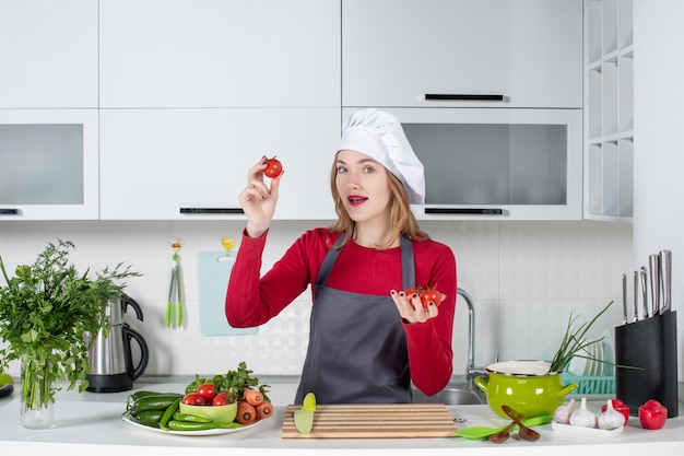 Vista frontal agradable cocinera en delantal sosteniendo tomates