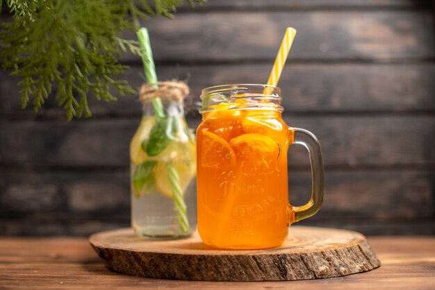 Vista frontal de agua de desintoxicación y jugo fresco en botellas con tubos sobre fondo de madera marrón