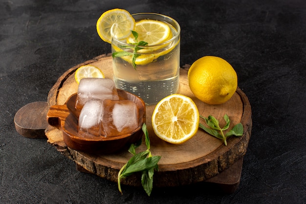 Una vista frontal de agua con limón bebida fresca fresca dentro de un vaso con cubitos de hielo con limones en rodajas en la oscuridad