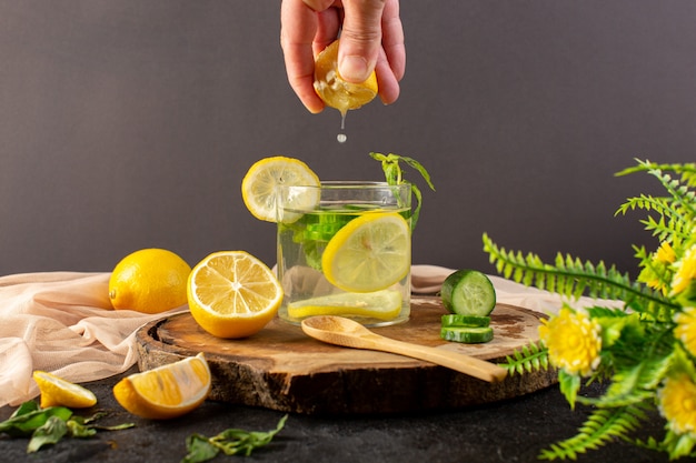 Una vista frontal de agua con limón bebida fresca y fresca dentro del vaso obteniendo un poco de jugo de limón con cubitos de hielo rodajas de limones pepino en la oscuridad