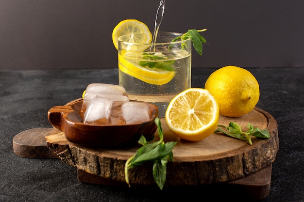 Una vista frontal de agua con limón fresca bebida fresca dentro de un vaso con cubitos de hielo con limones en rodajas en la oscuridad