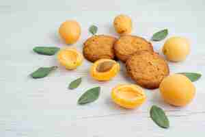Foto gratuita una vista frontal de albaricoques naranjas enteros y aromatizados con hojas verdes y galletas en el escritorio de luz