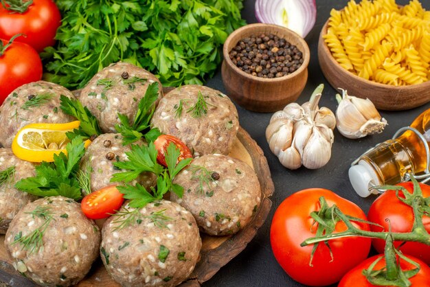 Vista frontal de albóndigas crudas en una tabla de cortar de madera y verduras frescas pastas verdes botella de aceite caída sobre fondo oscuro