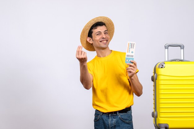 Vista frontal alegre joven turista en camiseta amarilla de pie junto a la maleta amarilla