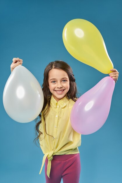 Vista frontal de la alegre niña manteniendo globos de colores