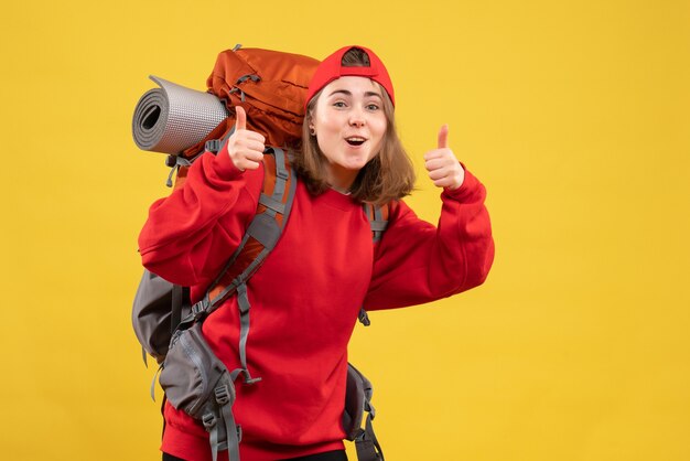 Vista frontal alegre viajero femenino con mochila dando pulgar hacia arriba