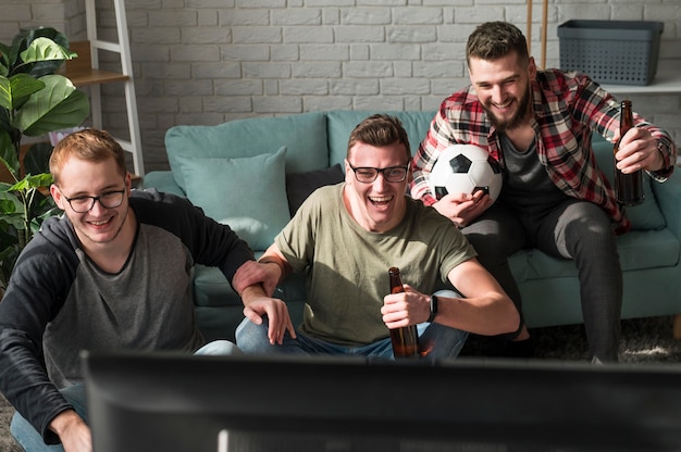 Vista frontal de alegres amigos varones viendo deportes en la televisión con fútbol