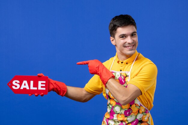 Vista frontal ama de llaves masculina dichosa en camiseta amarilla con cartel de venta en espacio azul