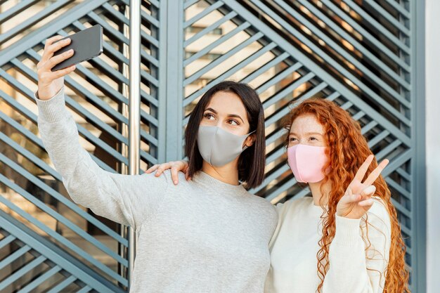 Vista frontal de amigas con máscaras faciales al aire libre tomando un selfie